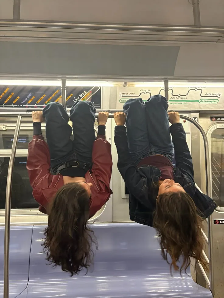Two friends hanging upside down from the rail of a late train