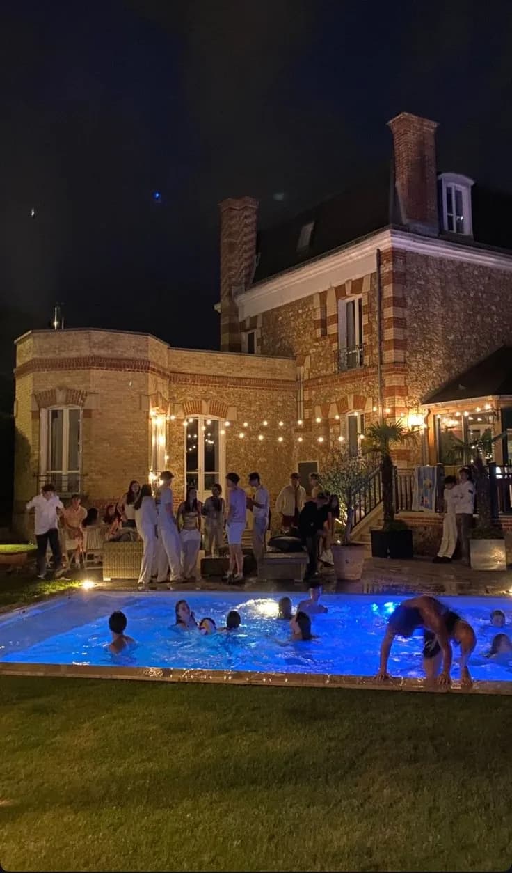 A pool party at night in front of a lit house